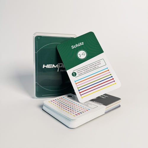 Eine Verpackung von HEMPEL The Game neben einem offenen Stapel des Spiels